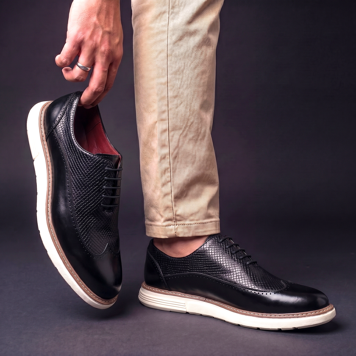 Men's Faux Leather Textured Wingtip Brogue Shoes in Black – worn and held side view | Hensley London