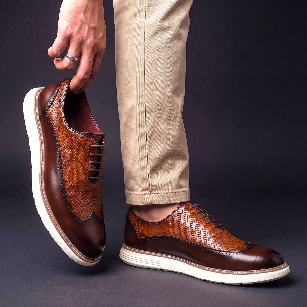 Men's Faux Leather Textured Wingtip Brogue Shoes in Brown – worn and held side view | Hensley London