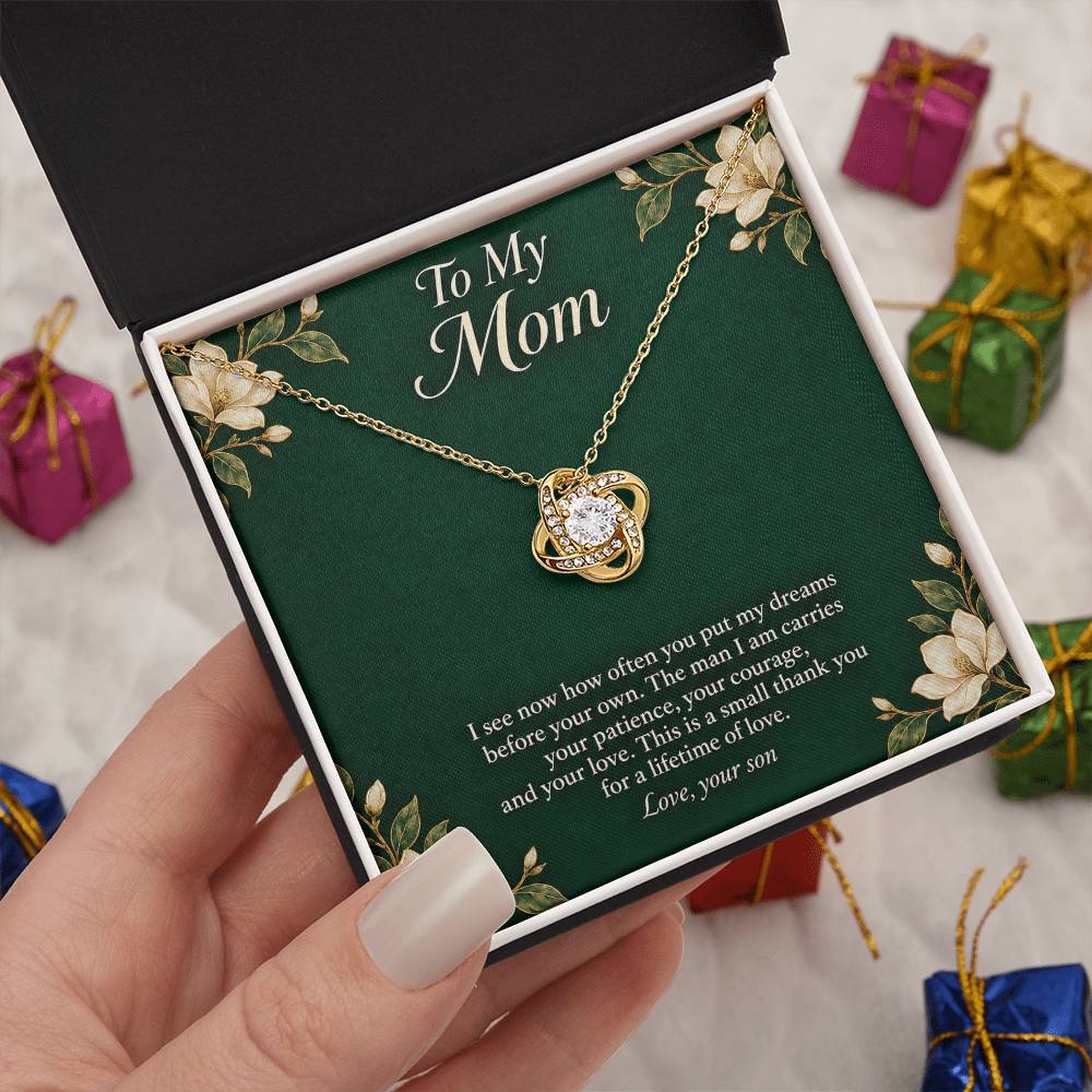 Yellow-gold Love Knot necklace and emerald Mom message card in standard box held in hand | Hensley London